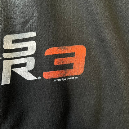 Gears of War 3 Marcus Fenix 2010 Promo Hoodie is a black zip-up hoodie with a dark Crimson Omen logo in orange tones on the left upper chest and a bloody Delta-One logo on one sleeve. The back features a large Marcus Fenix graphic with “Gears of War 3” text below it and a small 2010 Epic Games licensing mark.