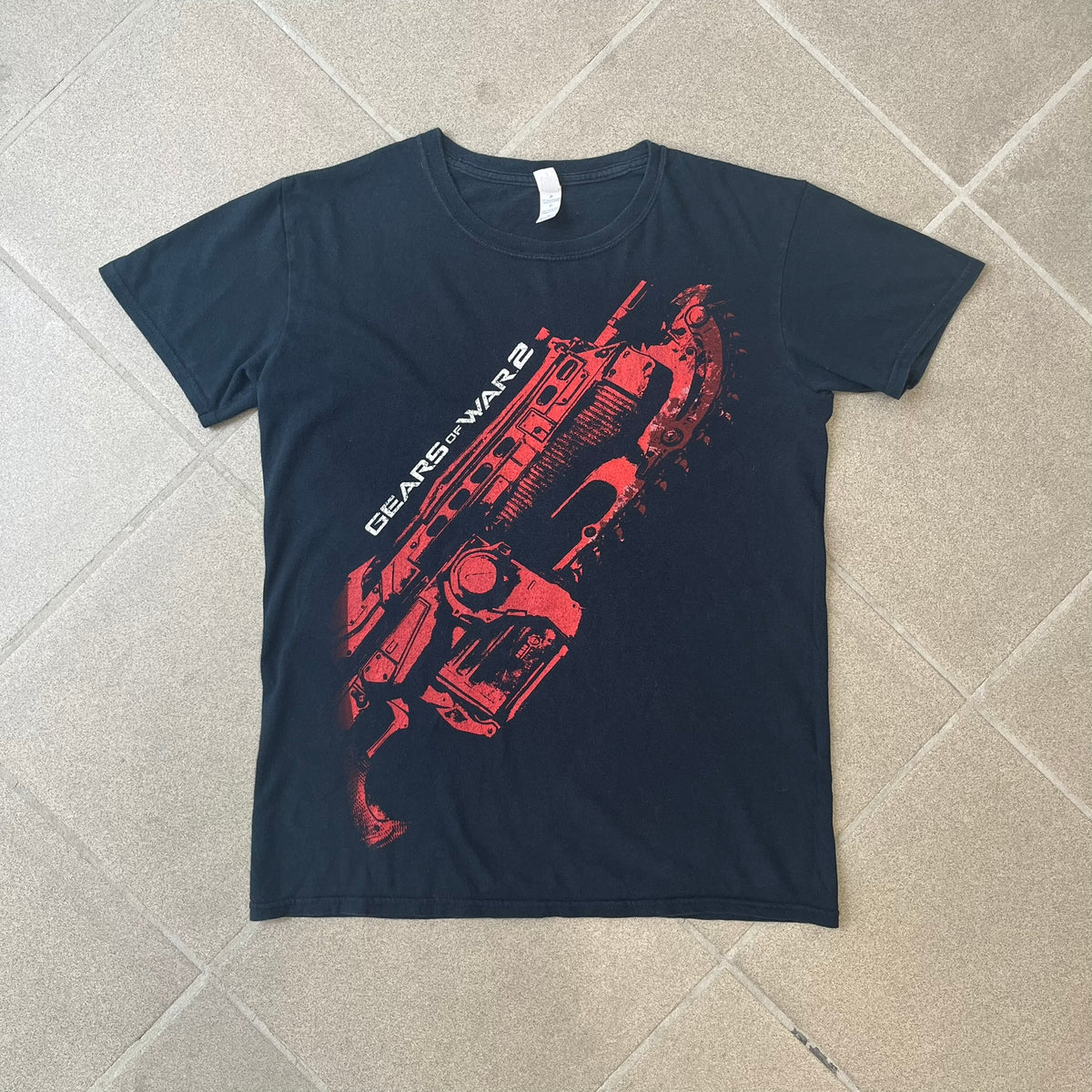 Gears of War 2 2008 Red Lancer Tee is a black, 100% cotton T-shirt featuring a large red Lancer graphic on the front alongside small white "Gears of War 2" text. The upper back displays the GOW2 skull logo with 2008 licensing below.