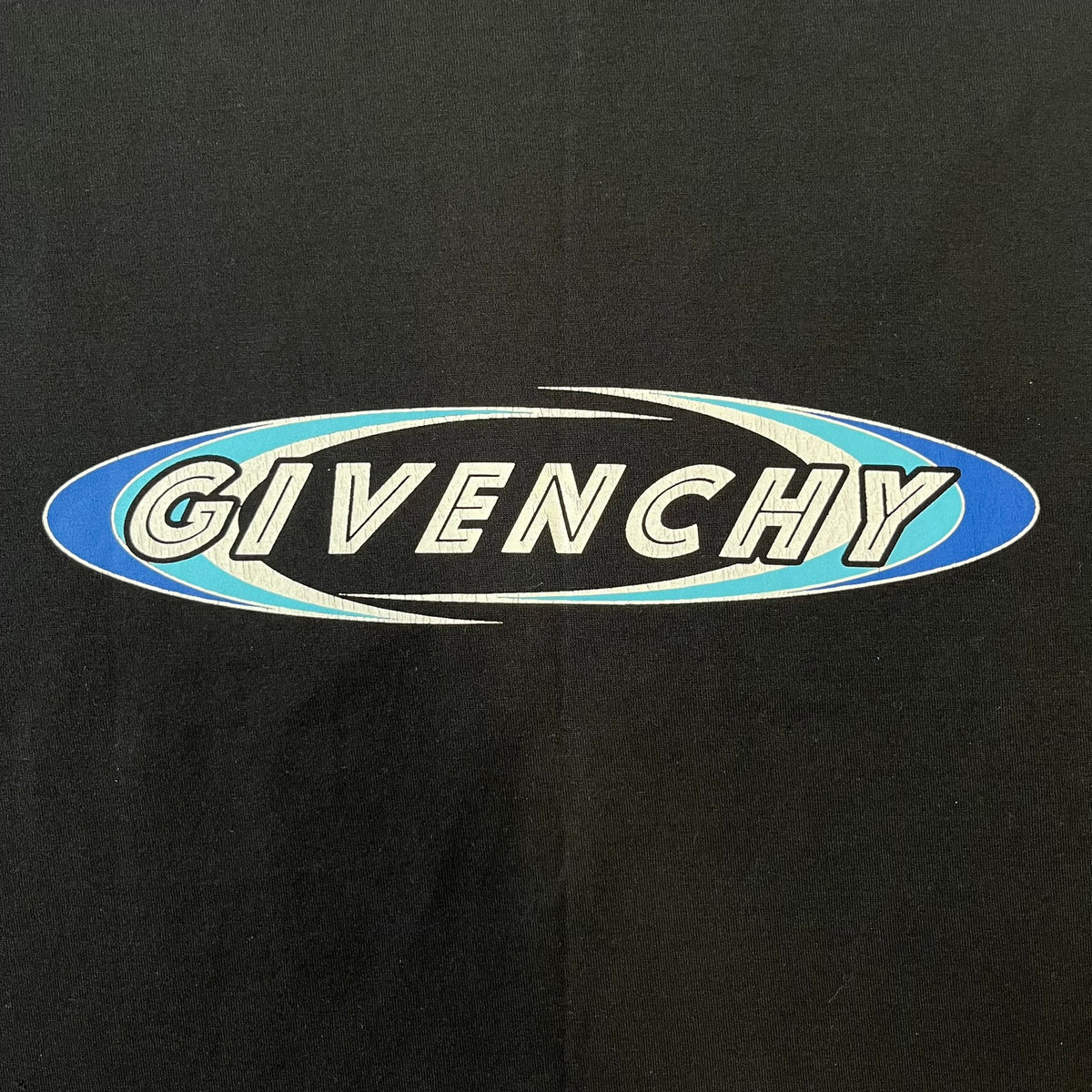 Givenchy AW18 Aquarius Black Tee is a black, slim-fit T-shirt made from 100% cotton, featuring white "GIVENCHY" text on the front alongside a blue half-moon-shaped graphics. The back displays an Aquarius-inspired design in white, gray, and blue, depicting a fountain with a large bird, a cube built from repeated Givenchy logos, and a Givenchy signature.