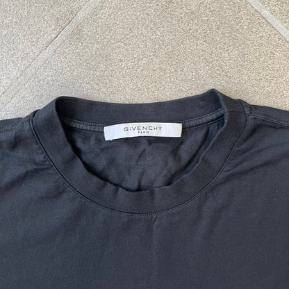 Givenchy AW18 Aquarius Black Tee is a black, slim-fit T-shirt made from 100% cotton, featuring white "GIVENCHY" text on the front alongside a blue half-moon-shaped graphics. The back displays an Aquarius-inspired design in white, gray, and blue, depicting a fountain with a large bird, a cube built from repeated Givenchy logos, and a Givenchy signature.