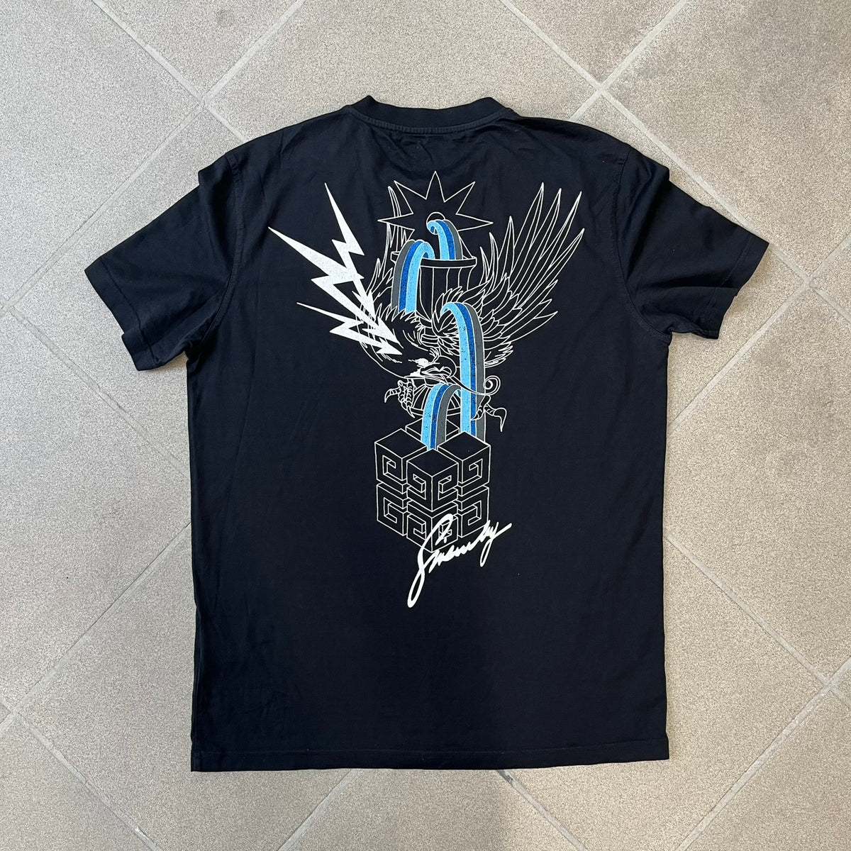 Givenchy AW18 Aquarius Black Tee is a black, slim-fit T-shirt made from 100% cotton, featuring white "GIVENCHY" text on the front alongside a blue half-moon-shaped graphics. The back displays an Aquarius-inspired design in white, gray, and blue, depicting a fountain with a large bird, a cube built from repeated Givenchy logos, and a Givenchy signature.
