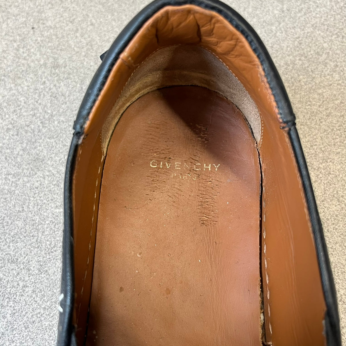 Givenchy Black & White Stars Slip-On Sneakers are made in Italy from premium black leather, featuring a white sole and a black upper detailed with a white outlined pattern of Givenchy text and stars. The interior is finished in brown, with a small Givenchy logo placed on the back of the sole.
