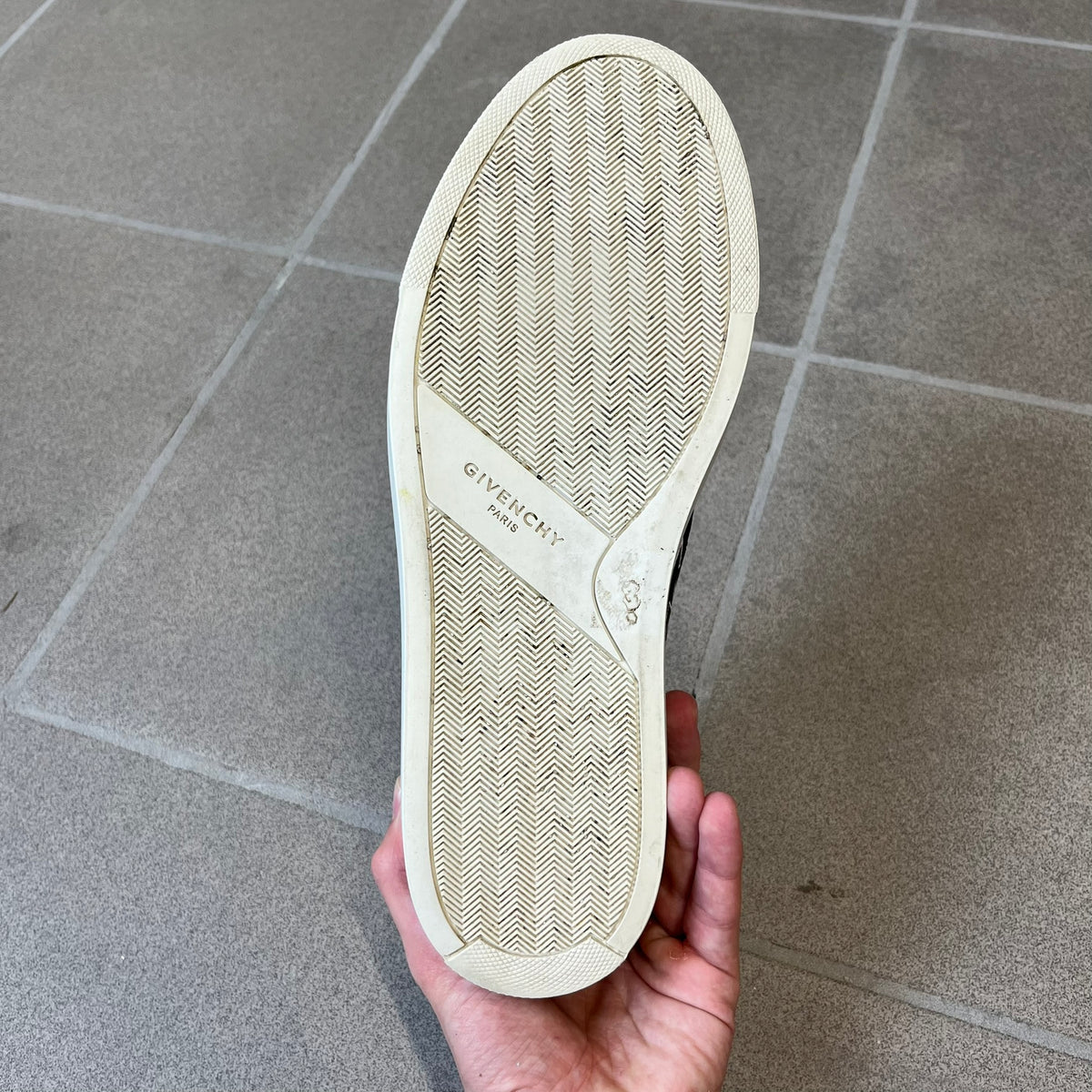 Givenchy Black & White Stars Slip-On Sneakers are made in Italy from premium black leather, featuring a white sole and a black upper detailed with a white outlined pattern of Givenchy text and stars. The interior is finished in brown, with a small Givenchy logo placed on the back of the sole.