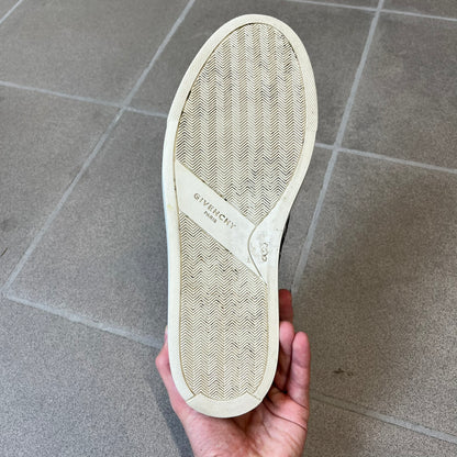 Givenchy Black & White Stars Slip-On Sneakers are made in Italy from premium black leather, featuring a white sole and a black upper detailed with a white outlined pattern of Givenchy text and stars. The interior is finished in brown, with a small Givenchy logo placed on the back of the sole.