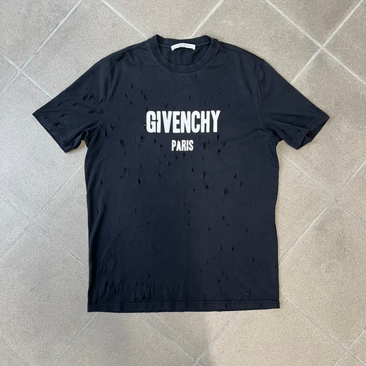 Givenchy Distressed Logo Paris Tee is a black T-shirt made from 100% cotton in Portugal, featuring white "GIVENCHY" text on the chest with "PARIS" printed below it. The shirt is finished with an all-over factory-distressed design, with holes intentionally placed across both the front and back.