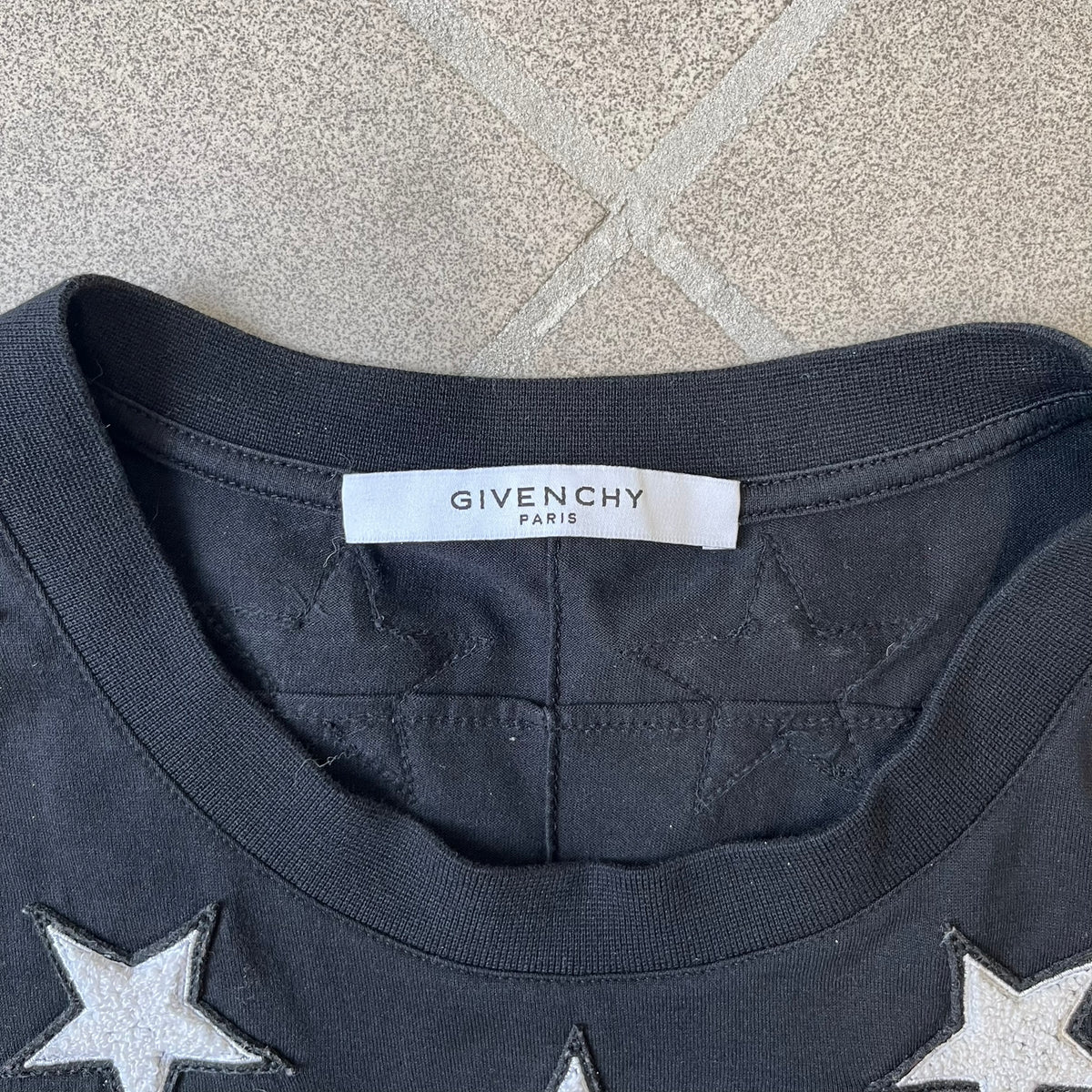 Givenchy 2017 Black Star Patch 4-7 Tee is a black, Cuban-fit T-shirt made from 100% cotton, featuring fuzzy white star patches trimming the collar on both the front and back. White "4" and "7" numbering is printed on the sleeves.