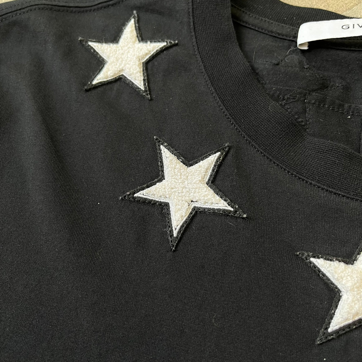 Givenchy 2017 Black Star Patch 4-7 Tee is a black, Cuban-fit T-shirt made from 100% cotton, featuring fuzzy white star patches trimming the collar on both the front and back. White "4" and "7" numbering is printed on the sleeves.