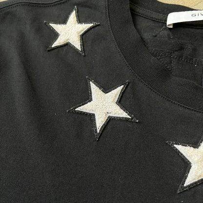 Givenchy 2017 Black Star Patch 4-7 Tee is a black, Cuban-fit T-shirt made from 100% cotton, featuring fuzzy white star patches trimming the collar on both the front and back. White "4" and "7" numbering is printed on the sleeves.