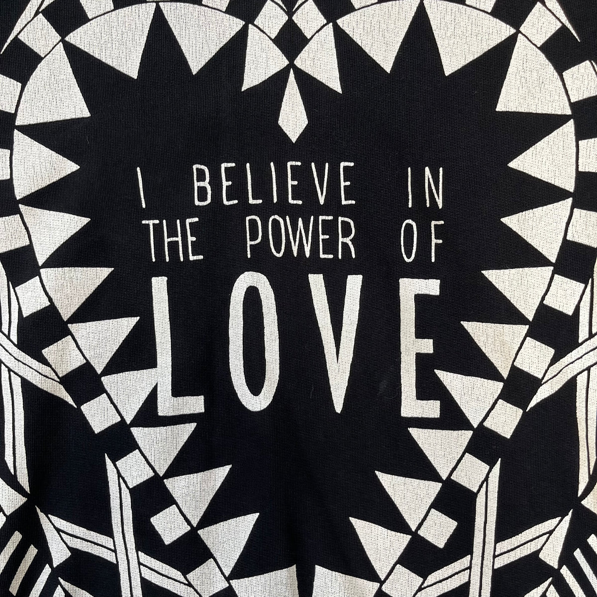 Givenchy FW16 "I Believe in the Power of Love" Crewneck is a black crewneck made from 100% cotton, featuring a white graphic heart built from varying patterns that grow from small to large, with "I Believe in the Power of Love" text placed at its center.&nbsp;