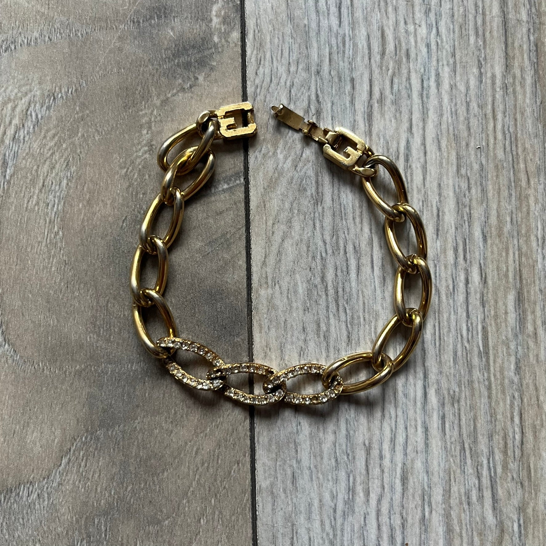 The Givenchy Gold-Tone Crystal Pavé Link Bracelet features a gold-tone Pavé Link chain with larger circular end links connecting to the clasp. The 3 middle links have embedded crystals. The foldover clasp is stamped Givenchy Paris New York. Vintage piece with a consistent gold-tone finish.