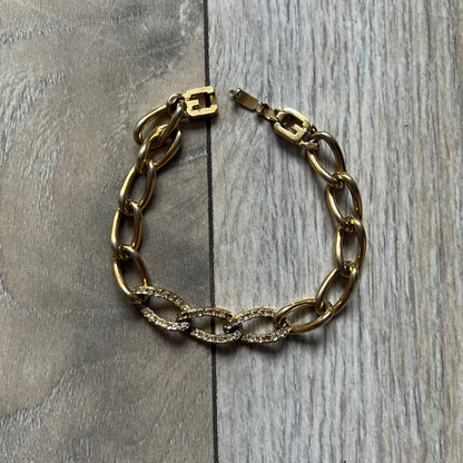 The Givenchy Gold-Tone Crystal Pavé Link Bracelet features a gold-tone Pavé Link chain with larger circular end links connecting to the clasp. The 3 middle links have embedded crystals. The foldover clasp is stamped Givenchy Paris New York. Vintage piece with a consistent gold-tone finish.