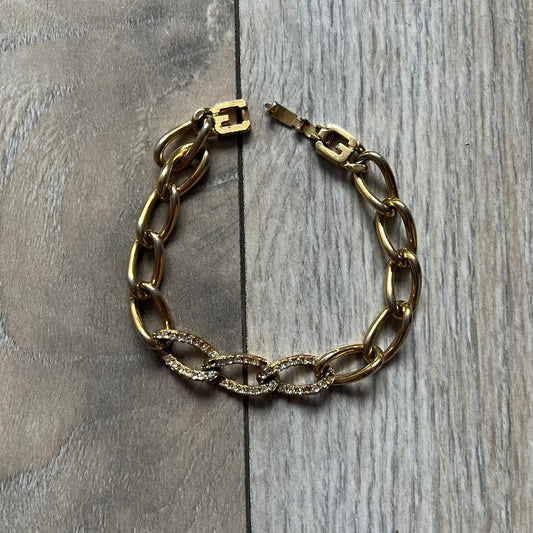 The Givenchy Gold-Tone Crystal Pavé Link Bracelet features a gold-tone Pavé Link chain with larger circular end links connecting to the clasp. The 3 middle links have embedded crystals. The foldover clasp is stamped Givenchy Paris New York. Vintage piece with a consistent gold-tone finish.