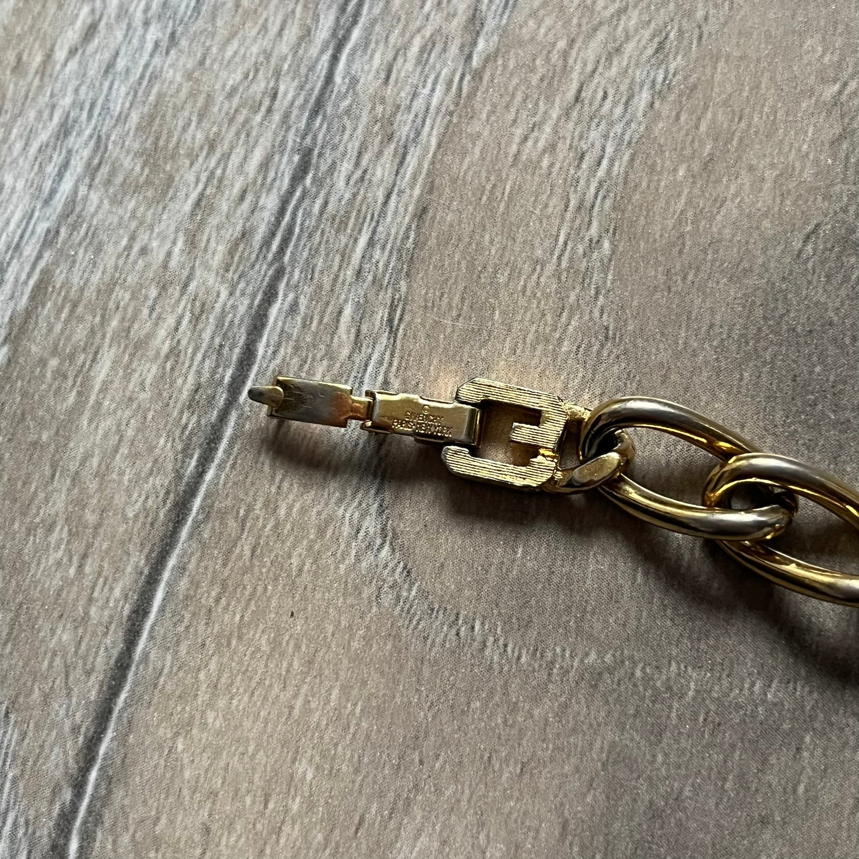 The Givenchy Gold-Tone Crystal Pavé Link Bracelet features a gold-tone Pavé Link chain with larger circular end links connecting to the clasp. The 3 middle links have embedded crystals. The foldover clasp is stamped Givenchy Paris New York. Vintage piece with a consistent gold-tone finish.