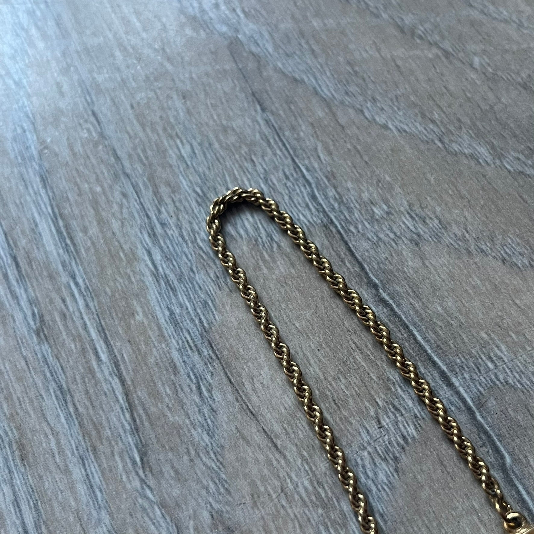 The Givenchy Gold-Tone Vintage Rope Bracelet features a thin gold-tone rope-style chain with larger circular end links shaped like the Givenchy “G” connecting to the clasp. The foldover clasp is oversized compared to the chain and is stamped Givenchy Paris New York. Vintage piece with a uniform gold-tone finish.