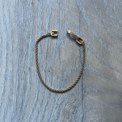The Givenchy Gold-Tone Vintage Rope Bracelet features a thin gold-tone rope-style chain with larger circular end links shaped like the Givenchy “G” connecting to the clasp. The foldover clasp is oversized compared to the chain and is stamped Givenchy Paris New York. Vintage piece with a uniform gold-tone finish.