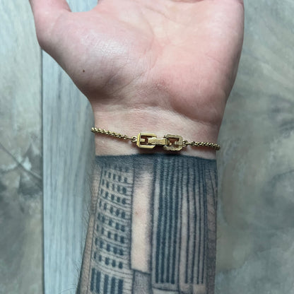 The Givenchy Gold-Tone Vintage Rope Bracelet features a thin gold-tone rope-style chain with larger circular end links shaped like the Givenchy “G” connecting to the clasp. The foldover clasp is oversized compared to the chain and is stamped Givenchy Paris New York. Vintage piece with a uniform gold-tone finish.