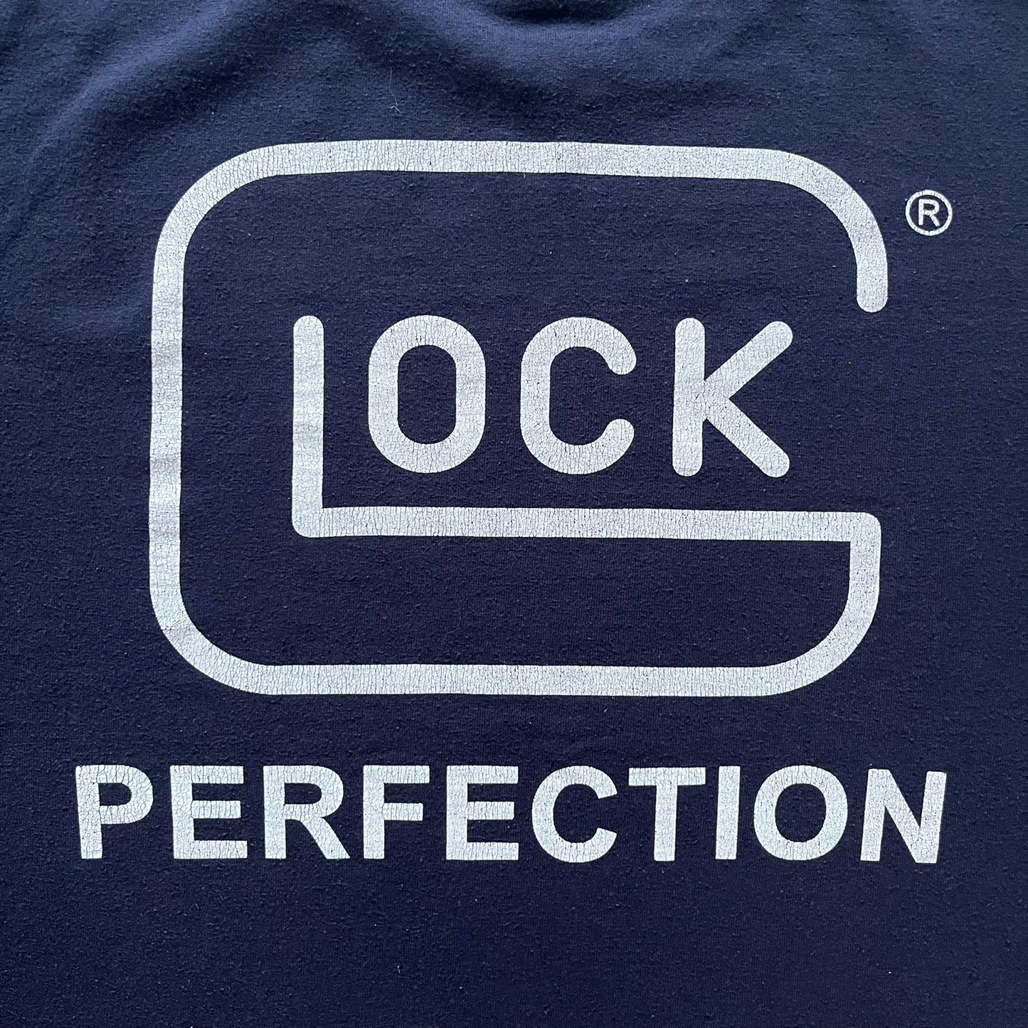 Navy Glock Perfection Tee from the 2000s, made on a Hanes Heavyweight 50/50 cotton-poly blend. Features a large white Glock Perfection logo on the back and a smaller matching logo on the left chest. Thick, high-quality construction.