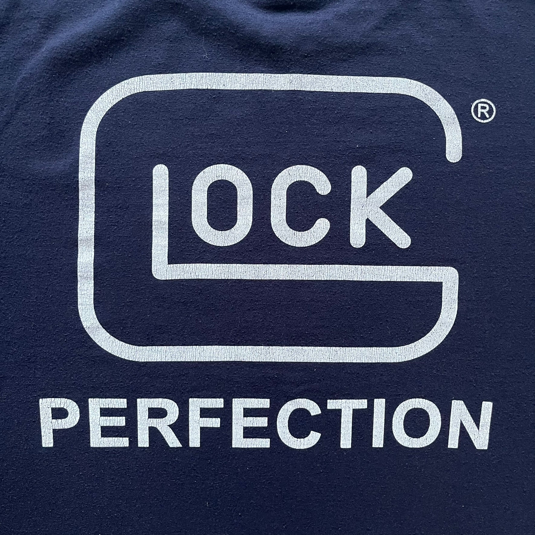 Navy Glock Perfection Tee from the 2000s, made on a Hanes Heavyweight 50/50 cotton-poly blend. Features a large white Glock Perfection logo on the back and a smaller matching logo on the left chest. Thick, high-quality construction.