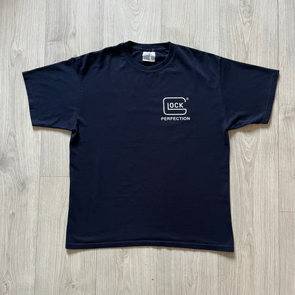 Navy Glock Perfection Tee from the 2000s, made on a Hanes Heavyweight 50/50 cotton-poly blend. Features a large white Glock Perfection logo on the back and a smaller matching logo on the left chest. Thick, high-quality construction.