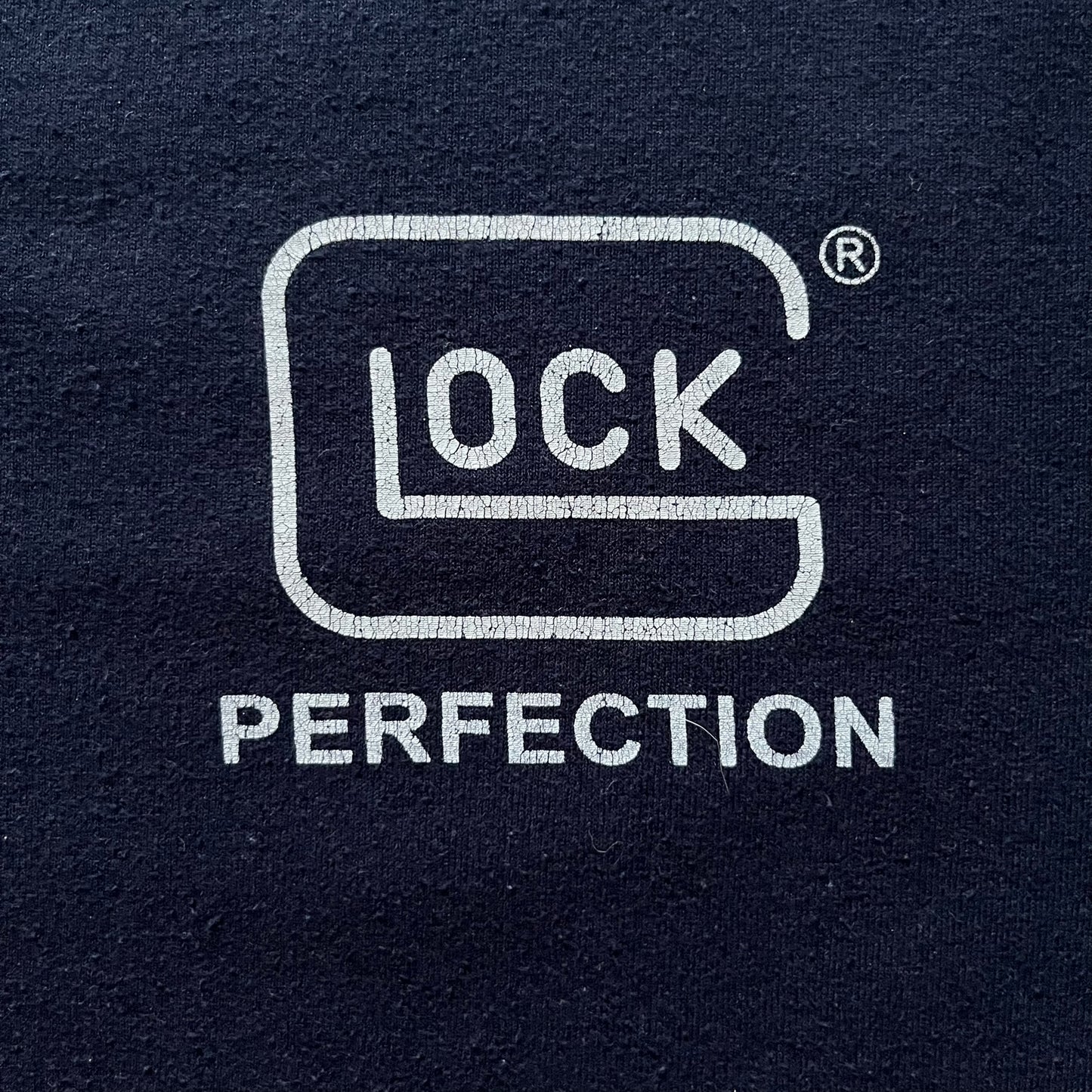 Navy Glock Perfection Tee from the 2000s, made on a Hanes Heavyweight 50/50 cotton-poly blend. Features a large white Glock Perfection logo on the back and a smaller matching logo on the left chest. Thick, high-quality construction.