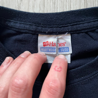 Navy Glock Perfection Tee from the 2000s, made on a Hanes Heavyweight 50/50 cotton-poly blend. Features a large white Glock Perfection logo on the back and a smaller matching logo on the left chest. Thick, high-quality construction.