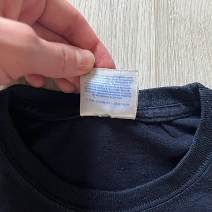 Navy Glock Perfection Tee from the 2000s, made on a Hanes Heavyweight 50/50 cotton-poly blend. Features a large white Glock Perfection logo on the back and a smaller matching logo on the left chest. Thick, high-quality construction.