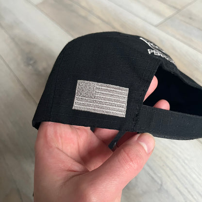 Glock Perfection USA Flag Baseball Cap is a black baseball cap featuring a fuzzy-style front patch with a white Glock Perfection logo. The left side has a silver USA flag patch, and the back is finished with an additional Glock Perfection logo. The cap has a classic curved brim and standard adjustable fit.