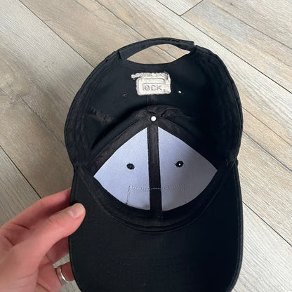 Glock Perfection USA Flag Baseball Cap is a black baseball cap featuring a fuzzy-style front patch with a white Glock Perfection logo. The left side has a silver USA flag patch, and the back is finished with an additional Glock Perfection logo. The cap has a classic curved brim and standard adjustable fit.