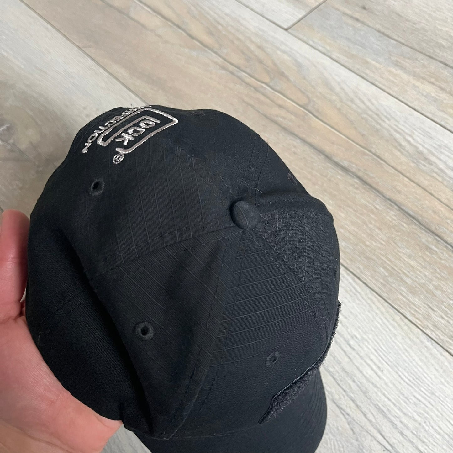 Glock Perfection USA Flag Baseball Cap is a black baseball cap featuring a fuzzy-style front patch with a white Glock Perfection logo. The left side has a silver USA flag patch, and the back is finished with an additional Glock Perfection logo. The cap has a classic curved brim and standard adjustable fit.