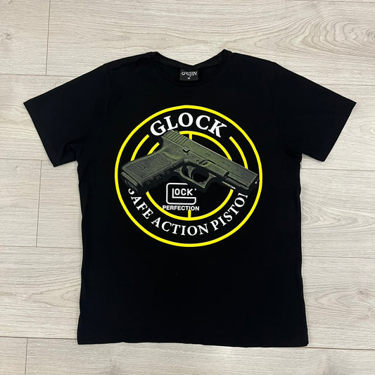 Glock Safe Action Pistol T-Shirt in black, made on an Orijin blank from 100% cotton. Features a large Glock pistol graphic on the front set inside a yellow circle, with “Glock Safe Action” text and Glock logo running around the graphic. The back has a white Glock logo printed below the collar.&nbsp;