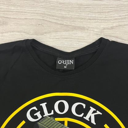 Glock Safe Action Pistol T-Shirt in black, made on an Orijin blank from 100% cotton. Features a large Glock pistol graphic on the front set inside a yellow circle, with “Glock Safe Action” text and Glock logo running around the graphic. The back has a white Glock logo printed below the collar.&nbsp;