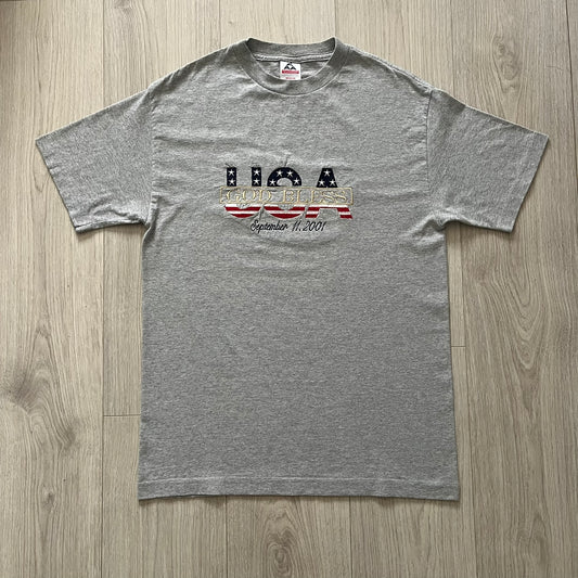Gray “God Bless USA” tee on an Alstyle blank, made from soft, durable cotton. Embroidery showcases USA in flag colors with gold “God Bless” text and a subtle September 11, 2001 detail underneath. A respectful and collectible commemorative shirt.