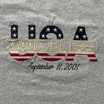 Gray “God Bless USA” tee on an Alstyle blank, made from soft, durable cotton. Embroidery showcases USA in flag colors with gold “God Bless” text and a subtle September 11, 2001 detail underneath. A respectful and collectible commemorative shirt.