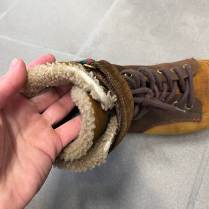 Gucci 2000’s Beige & Brown Shearling Lined Boots are made in Italy from beige and brown suede with a shearling-lined interior. A velcro strap with a Gucci logo closes the top, and the tongue has a leather tab with the Gucci logo. A green and red stripe runs around the top, a GG logo is on the side, and another GG logo appears on the sole along with a small one at the toe tip and a brown leather Gucci logo section on the sole. Due to age, the sole is falling apart and needs either gluing or a sole replacemen