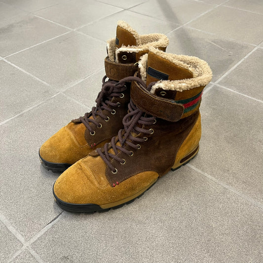 Gucci 2000’s Beige & Brown Shearling Lined Boots are made in Italy from beige and brown suede with a shearling-lined interior. A velcro strap with a Gucci logo closes the top, and the tongue has a leather tab with the Gucci logo. A green and red stripe runs around the top, a GG logo is on the side, and another GG logo appears on the sole along with a small one at the toe tip and a brown leather Gucci logo section on the sole. Due to age, the sole is falling apart and needs either gluing or a sole replacemen