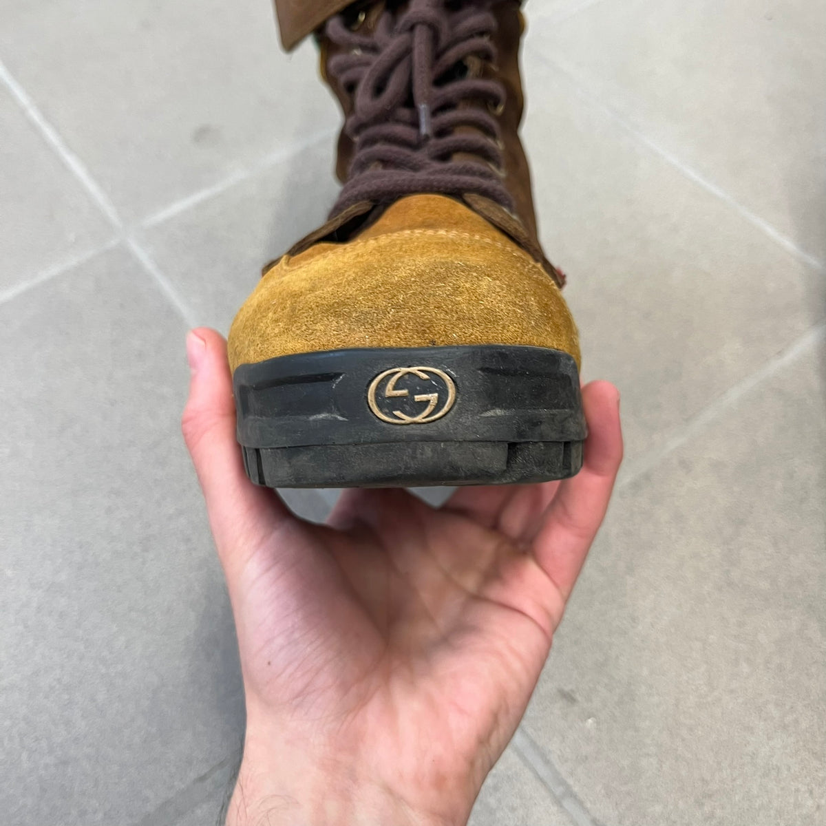 Gucci 2000’s Beige & Brown Shearling Lined Boots are made in Italy from beige and brown suede with a shearling-lined interior. A velcro strap with a Gucci logo closes the top, and the tongue has a leather tab with the Gucci logo. A green and red stripe runs around the top, a GG logo is on the side, and another GG logo appears on the sole along with a small one at the toe tip and a brown leather Gucci logo section on the sole. Due to age, the sole is falling apart and needs either gluing or a sole replacemen