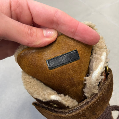 Gucci 2000’s Beige & Brown Shearling Lined Boots are made in Italy from beige and brown suede with a shearling-lined interior. A velcro strap with a Gucci logo closes the top, and the tongue has a leather tab with the Gucci logo. A green and red stripe runs around the top, a GG logo is on the side, and another GG logo appears on the sole along with a small one at the toe tip and a brown leather Gucci logo section on the sole. Due to age, the sole is falling apart and needs either gluing or a sole replacemen