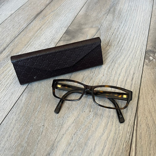 Gucci GG 3080 086 Glasses Frames are eyeglass frames made in Italy, featuring a brown and orange-toned acetate construction. The temples are detailed with silver GG monogram pattern accents and Gucci’s signature red and green web stripe near the front of the arms. The frames come with a matching monogram Gucci case.