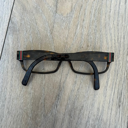 Gucci GG 3080 086 Glasses Frames are eyeglass frames made in Italy, featuring a brown and orange-toned acetate construction. The temples are detailed with silver GG monogram pattern accents and Gucci’s signature red and green web stripe near the front of the arms. The frames come with a matching monogram Gucci case.