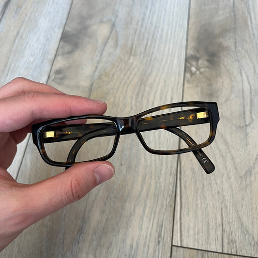 Gucci GG 3080 086 Glasses Frames are eyeglass frames made in Italy, featuring a brown and orange-toned acetate construction. The temples are detailed with silver GG monogram pattern accents and Gucci’s signature red and green web stripe near the front of the arms. The frames come with a matching monogram Gucci case.