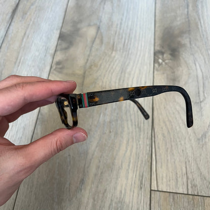 Gucci GG 3080 086 Glasses Frames are eyeglass frames made in Italy, featuring a brown and orange-toned acetate construction. The temples are detailed with silver GG monogram pattern accents and Gucci’s signature red and green web stripe near the front of the arms. The frames come with a matching monogram Gucci case.