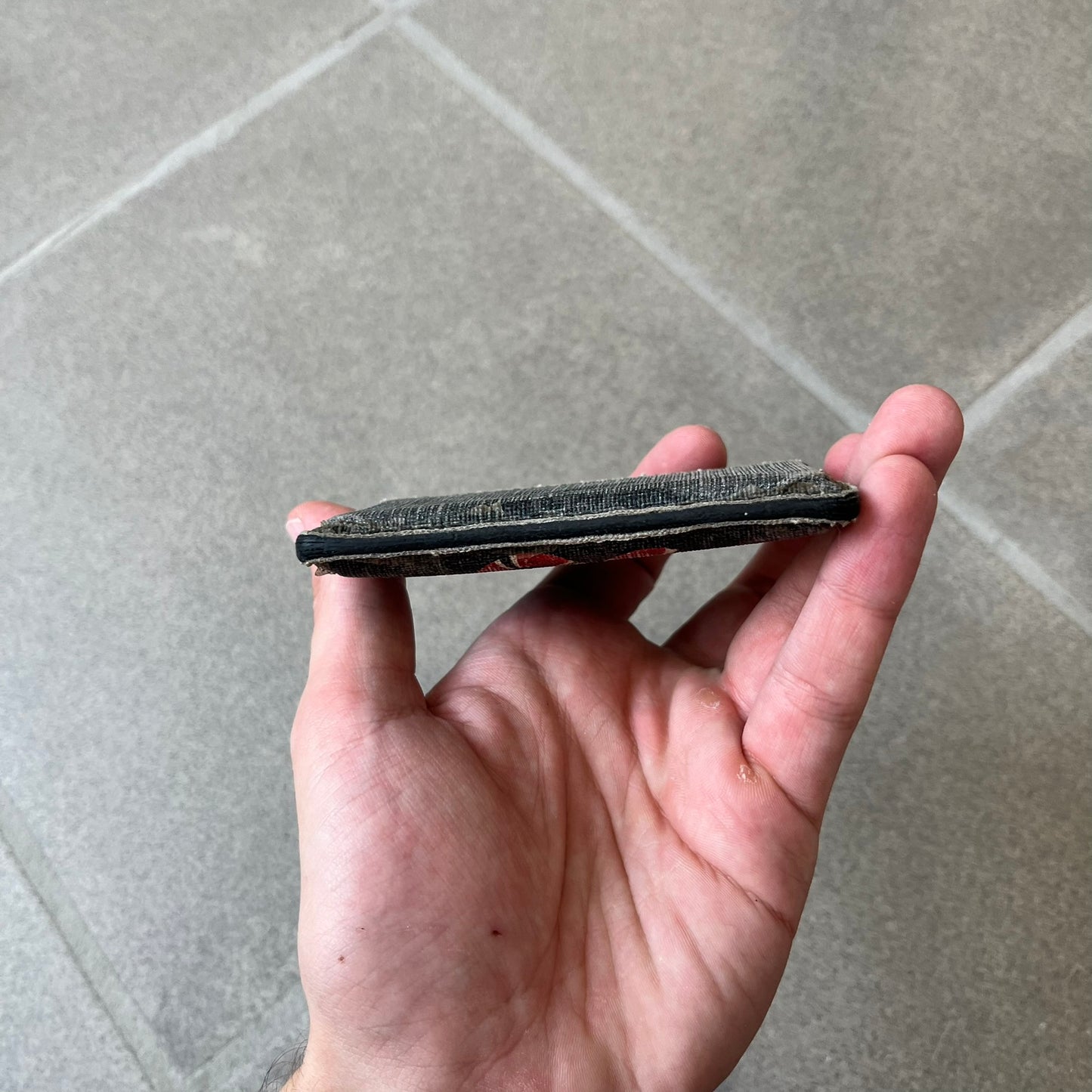 Gucci GG Supreme Kingsnake Card Holder features black and grey GG Supreme canvas with a red and black Kingsnake graphic and black leather trim. It has two card slots on the front, two on the back, and one central slot at the top.

