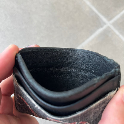 Gucci GG Supreme Kingsnake Card Holder features black and grey GG Supreme canvas with a red and black Kingsnake graphic and black leather trim. It has two card slots on the front, two on the back, and one central slot at the top.
