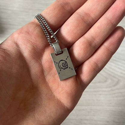 Hand holding a silver pendant with a skull design on a neutral background