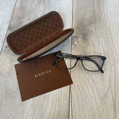 Gucci Gray-Blue Glasses Frames feature a translucent gray and dark blue acetate construction with a clear finish. Small silver GG logos are positioned on the front sides of the frames near the hinges. The frames are sold without lenses and come with a Gucci monogram case and a brown cleaning cloth.