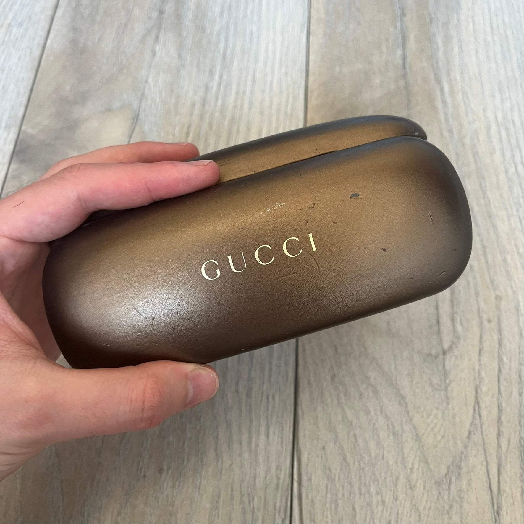 Gucci Gray-Blue Glasses Frames feature a translucent gray and dark blue acetate construction with a clear finish. Small silver GG logos are positioned on the front sides of the frames near the hinges. The frames are sold without lenses and come with a Gucci monogram case and a brown cleaning cloth.