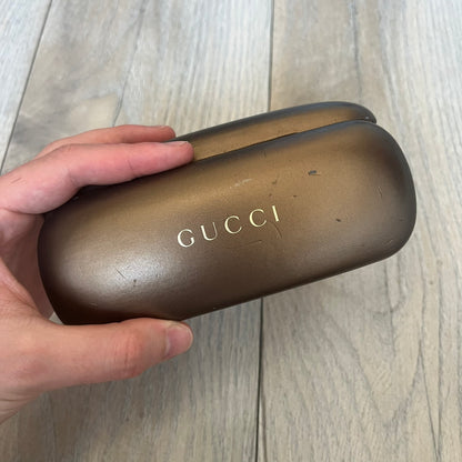 Gucci Gray-Blue Glasses Frames feature a translucent gray and dark blue acetate construction with a clear finish. Small silver GG logos are positioned on the front sides of the frames near the hinges. The frames are sold without lenses and come with a Gucci monogram case and a brown cleaning cloth.