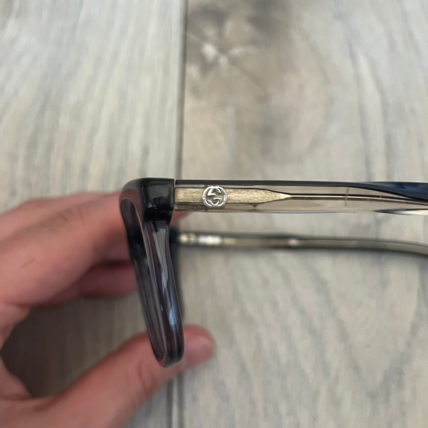 Gucci Gray-Blue Glasses Frames feature a translucent gray and dark blue acetate construction with a clear finish. Small silver GG logos are positioned on the front sides of the frames near the hinges. The frames are sold without lenses and come with a Gucci monogram case and a brown cleaning cloth.
