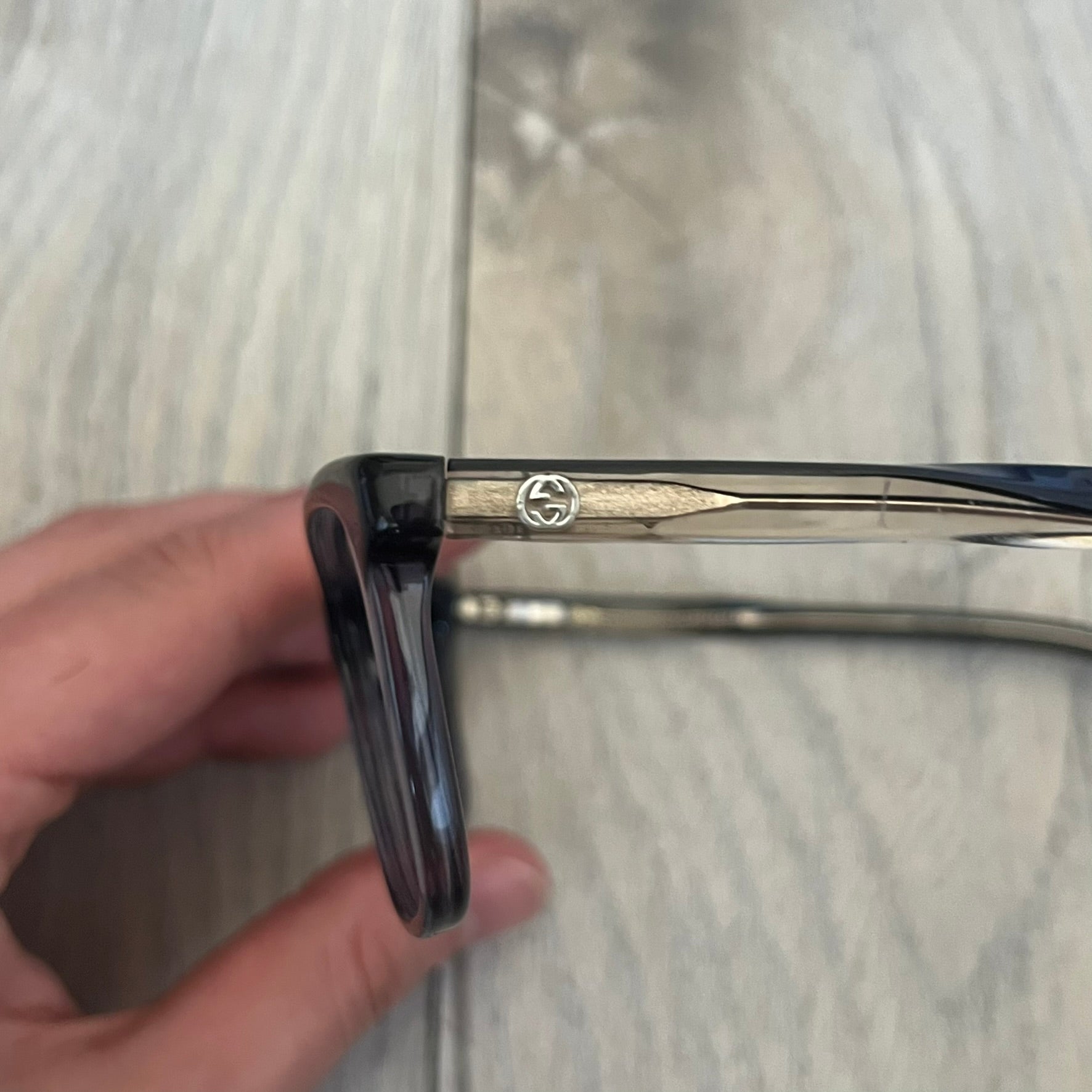 Gucci Gray-Blue Glasses Frames feature a translucent gray and dark blue acetate construction with a clear finish. Small silver GG logos are positioned on the front sides of the frames near the hinges. The frames are sold without lenses and come with a Gucci monogram case and a brown cleaning cloth.
