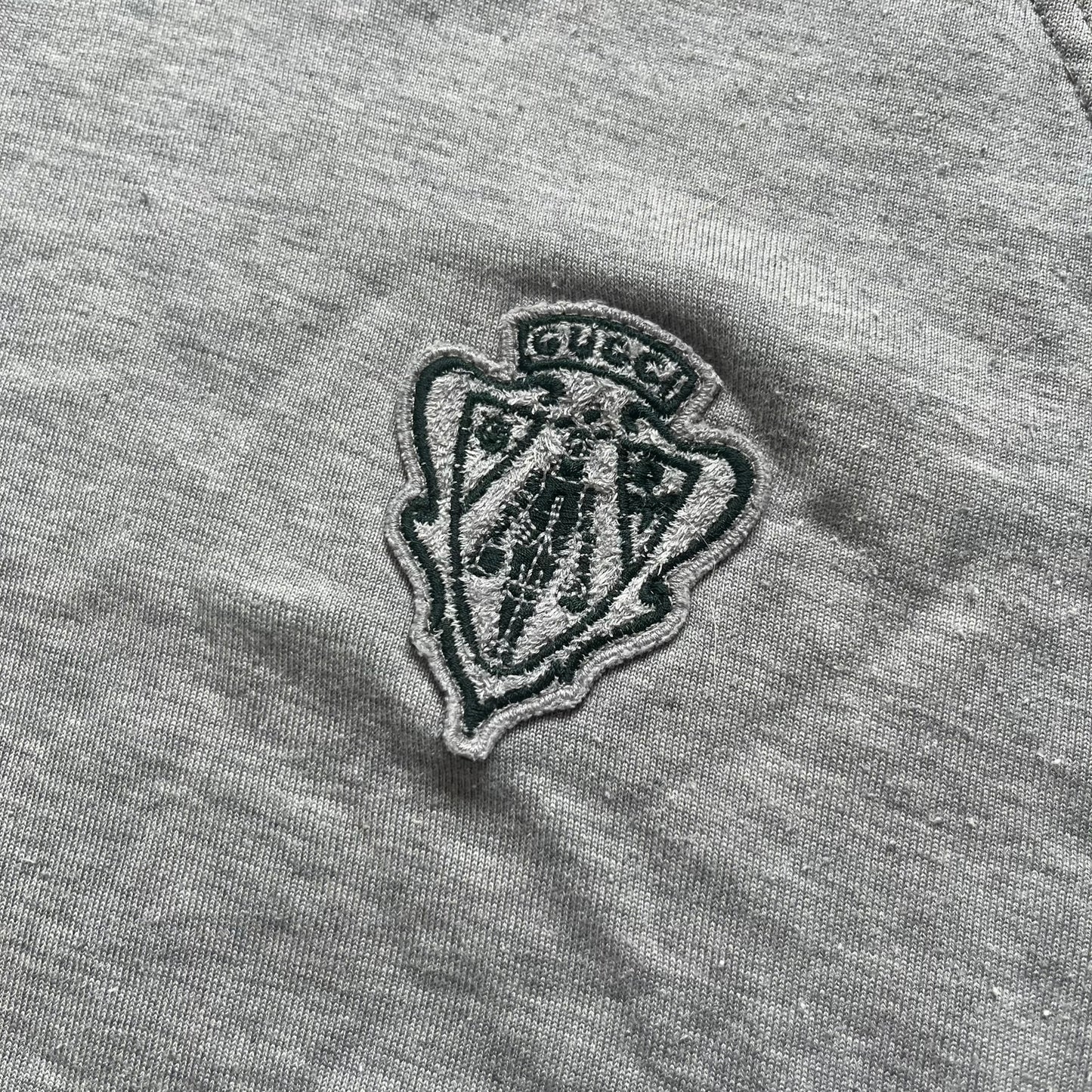 Gucci Gray Crest Patch Sherry Line Zip-Up Hoodie is a lightweight gray zip hoodie made in Italy. The chest features a crest patch with Gucci logo, while the bottom hem includes the green and red Web (Sherry Line) detail. The drawstrings have metal aglets engraved with Gucci branding.